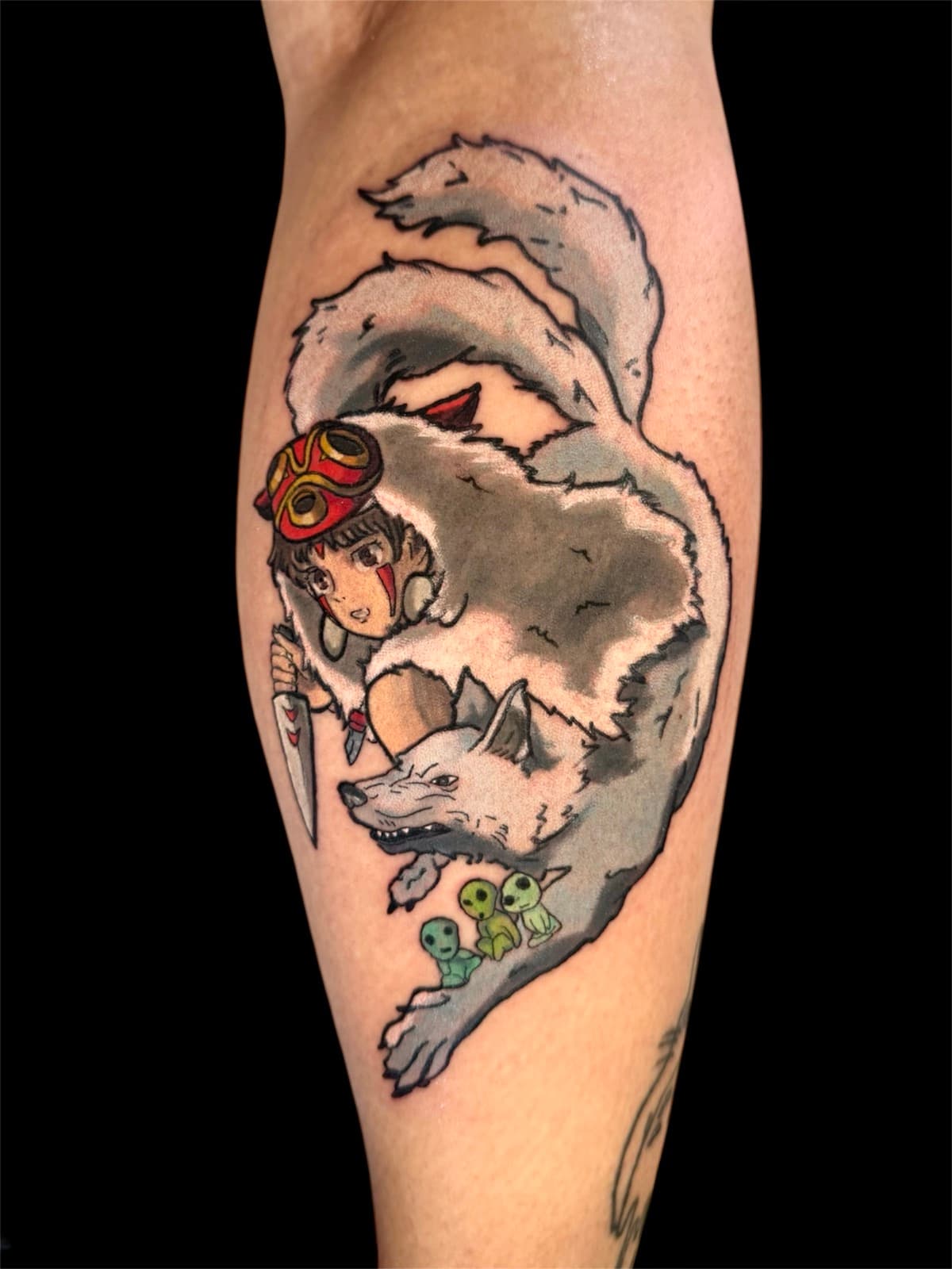 Princess Mononoke calf tattoo — San wearing her red mask and holding a knife, riding the white wolf goddess Moro, with three kodama forest spirits below.
