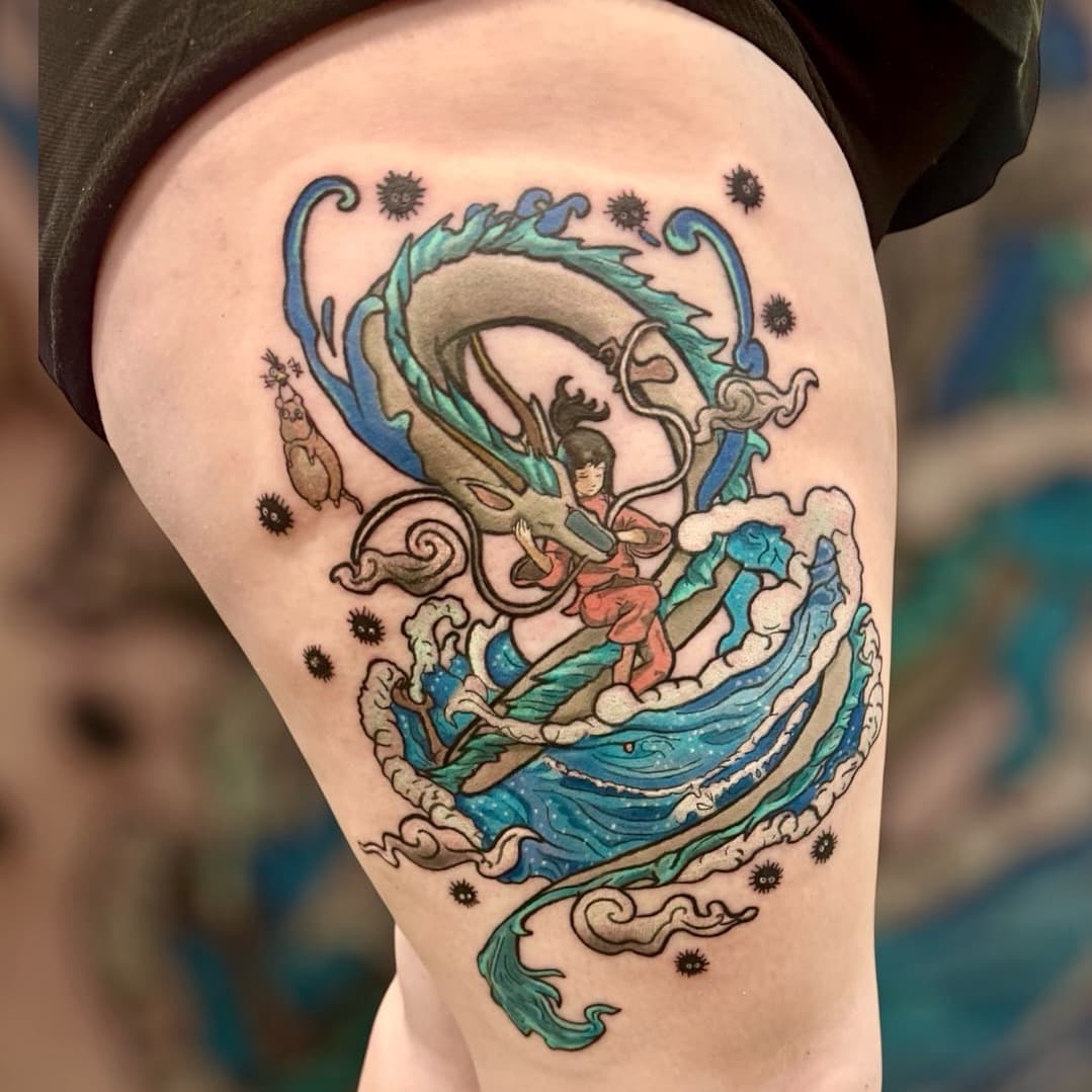 Spirited Away tattoo on thigh — Chihiro riding Haku in dragon form with soot sprites and ocean waves around them.