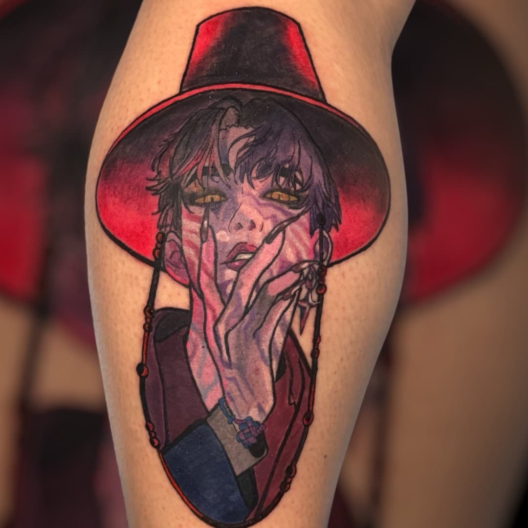 K-pop Demon Hunters Jinu calf tattoo — demon character portrait with purple hair, gold cat-slit eyes, red wide-brimmed hat, and hand raised near face.