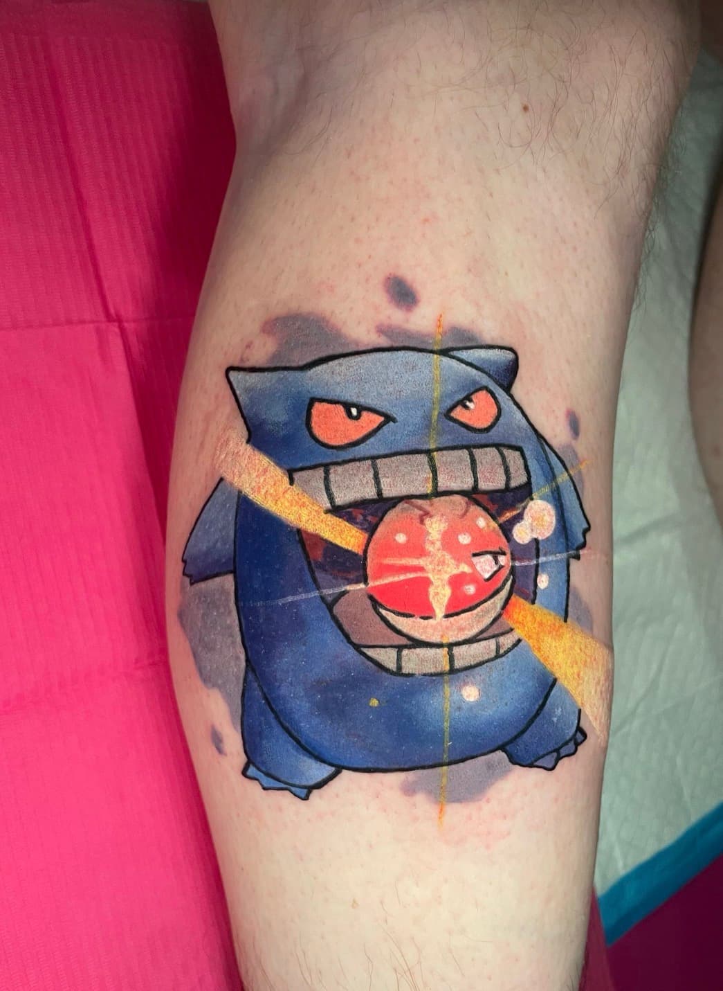 Watercolor Gengar Pokémon tattoo on calf with red Pokéball energy and purple watercolor splash.