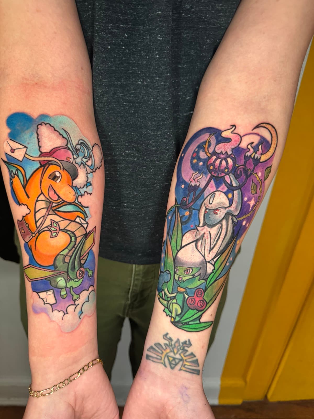 Two Pokémon forearm tattoos — left arm features Charmander with a mail satchel and clouds, right arm features Chandelure with purple flames over a grass-type Pokémon.