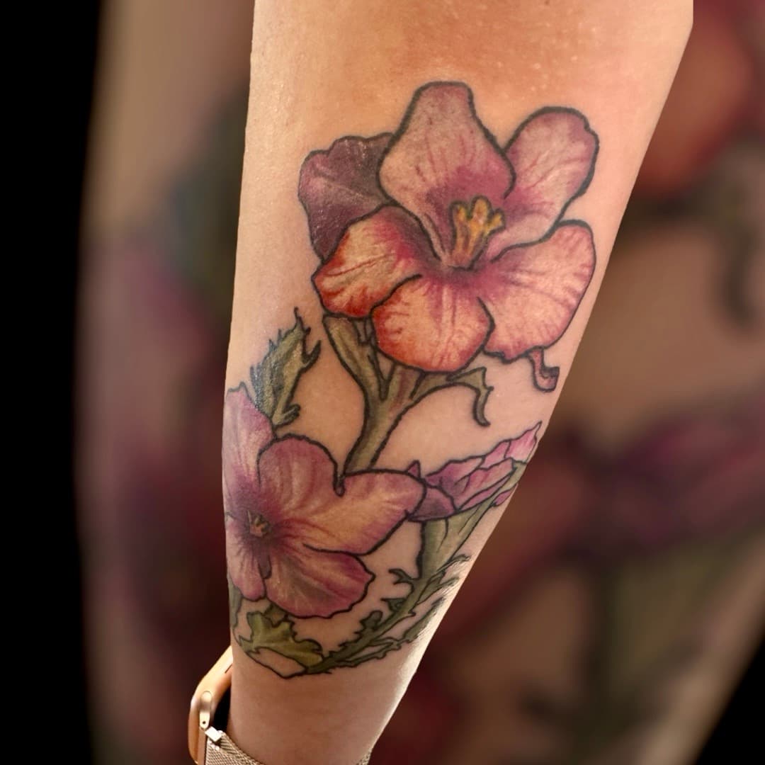 Illustrative pansy tattoo on forearm — pink and peach pansy flowers with purple shading and green leaves.