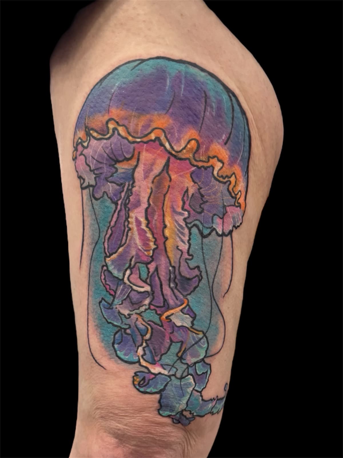Watercolor jellyfish tattoo on upper arm — purple and teal bell with pink and orange tentacles flowing downward.