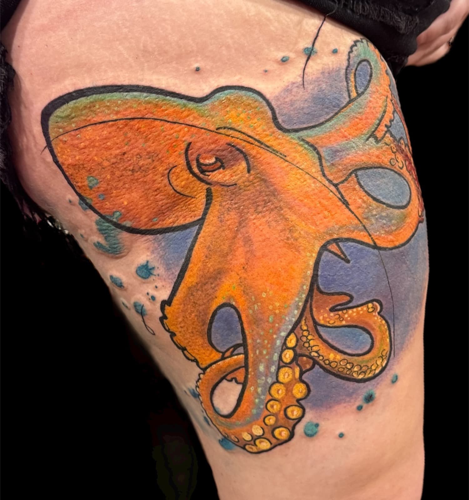 Vibrant watercolor octopus tattoo on thigh — orange body with teal blue splash background and yellow-gold suckers.