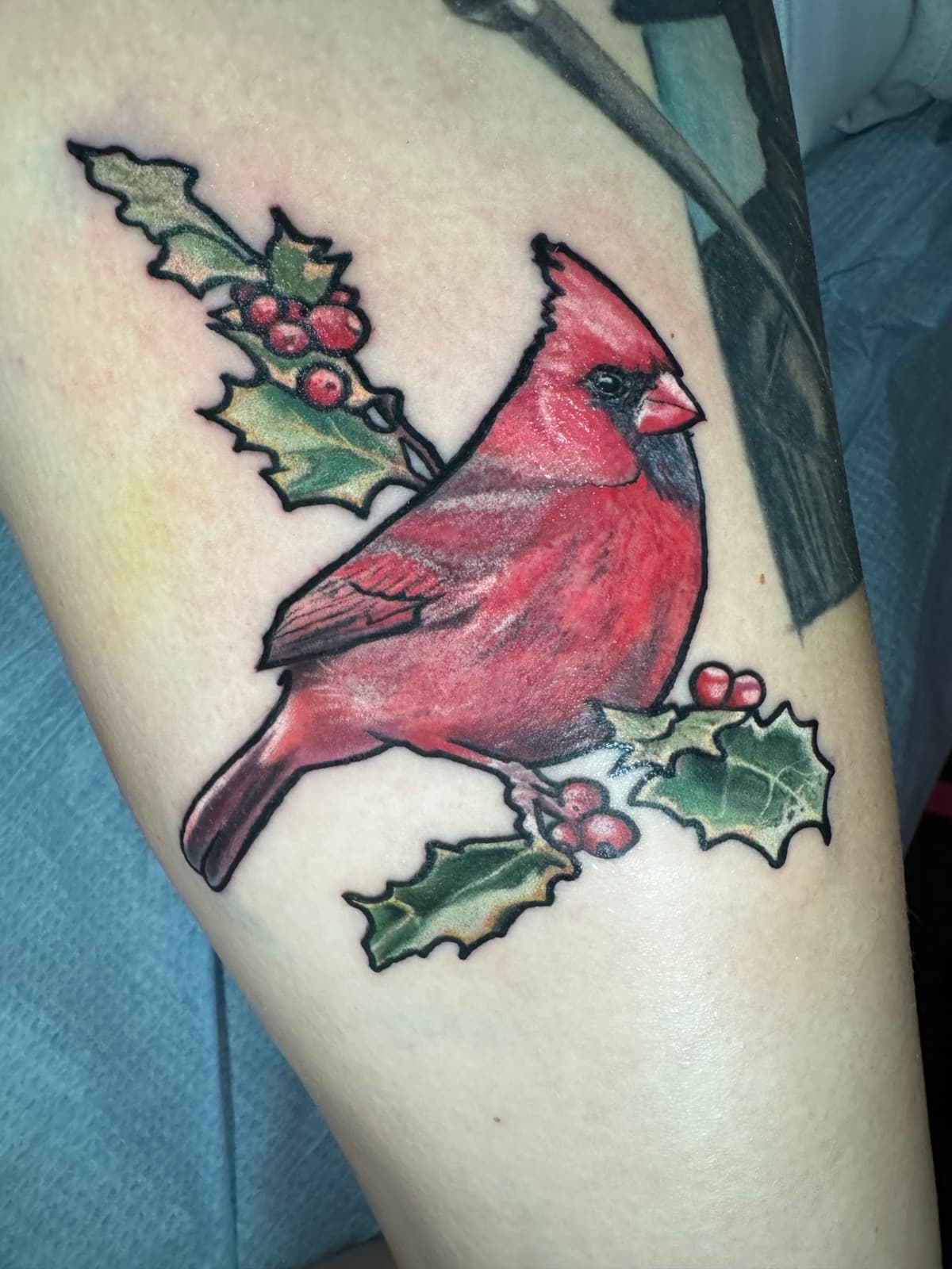 Color realism northern cardinal tattoo perched on a holly branch with red berries and green holly leaves.